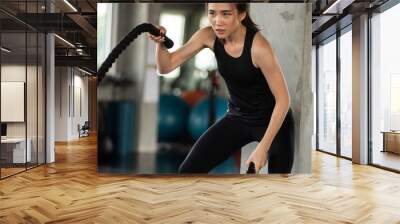 Athletic asian woman exercising with battle rope at gym Wall mural