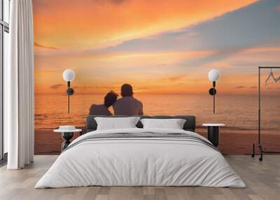 Couple in love watching sunset together on beach travel summer holidays. People silhouette from behind sitting enjoying view sunset sea on tropical destination vacation. Romantic couple on the beach Wall mural