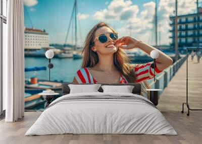 Elegant woman relaxing on outdoor deck of hotel looking at view of beach and sea. luxury travel on summer vacation. Stunning blond woman admiring coast town from her yacht,summer fashion. AI generated Wall mural