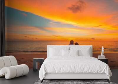 Romantic couple on the beach at colorful sunset on background. Beautiful tropical sunset scenery, romance couple sitting and watching the sunset sea and sky, horizon. Travel, honeymoon destination Wall mural