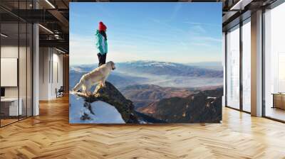 Girl with a golden retriever dog on top of a mountain during winter watching a beautiful landscape Wall mural