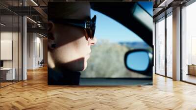 Pretty blonde caucasian woman driving a BMW car on a highway in Arizona (USA) wearing sunglasses and a black sweater Wall mural