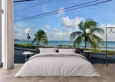 Small coastal street in Oistins, Barbados (Caribbean Island of the West Indies) with lush palm trees, a beautiful beach and the picturesque turquoise ocean in the background Wall mural