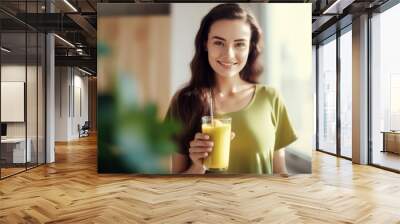 a cute girl with long hair in a green t-shirt stands by the window and holds a healthy natural smoothie in her hand Wall mural