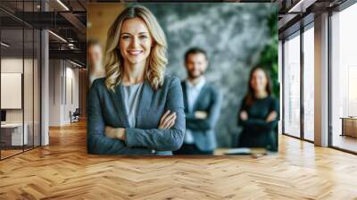 Confident businesswoman with arms crossed leading team in modern office, smiling female manager with colleagues in background, professional leadership in corporate setting Wall mural