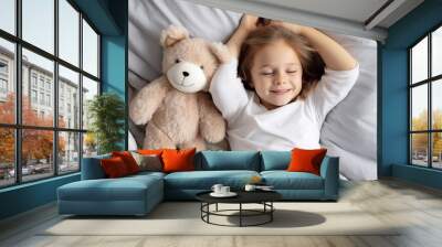 cute little girl lying with fluffy bear toy in cozy comfortable bed at home Wall mural