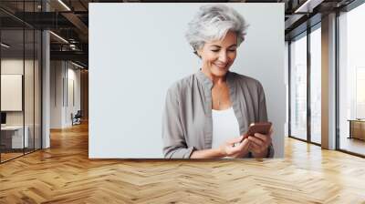 stylish senior woman with grey hair talking online using smartphone, modern lifestyle of the elderly, on light pastel background with copy space Wall mural