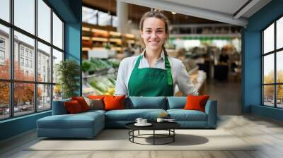 young girl with a green apron standing smiling at the camera at modern farmers market shop Wall mural