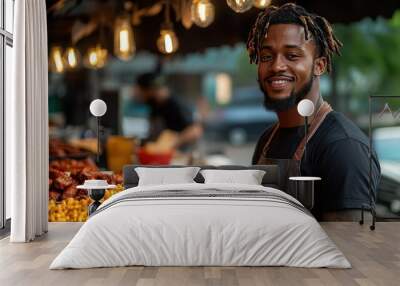 A smiling man with dreadlocks wearing a black shirt and apron stands in front of a food stall, smiling at the camera. He is surrounded by food, including macaroni and cheese and fried chicken. Wall mural