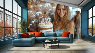 A young woman smiles happily as she holds a birthday cake with candles. Wall mural