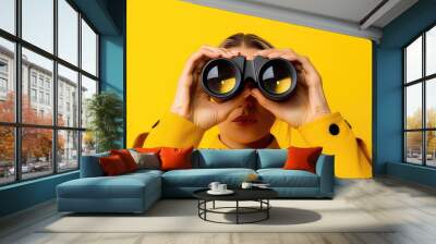 female hands hold black binoculars on a bright yellow background Wall mural