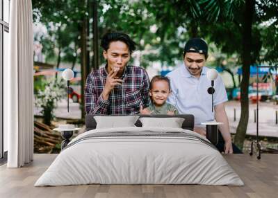 Two Southeast Asian men, close friends, chatting with one of their friend's child, Wall mural