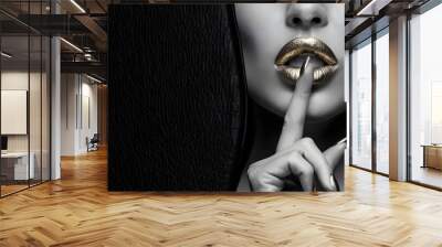 A striking black-and-white photograph featuring a woman's lips, painted boldly with gold lipstick. Her index finger, adorned with matching gold nail polish, is raised to her lip in a shushing gesture Wall mural