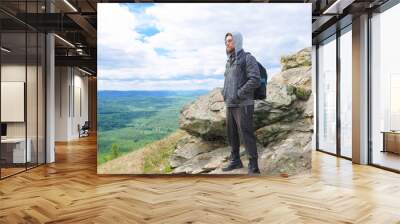 A man in a gray jacket stands on a mountain peak in full growth. Wall mural