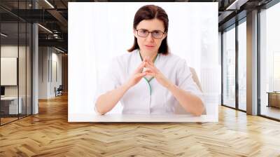 Beatiful female pediatrician sitting at her white table Wall mural