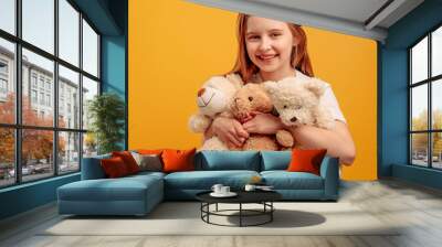 Beautiful girl child with three teddy bears isolated on yellow background with copyspace. Portrait of kid holding toys and smiling looking at the camera Wall mural