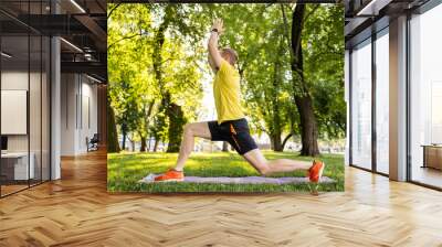 Man doing morning yoga at park outdoors in summer time. Guy exercising and stretch his body at nature in sunny day Wall mural