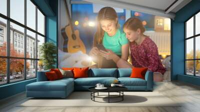 Sisters using smart phone at home in evening Wall mural