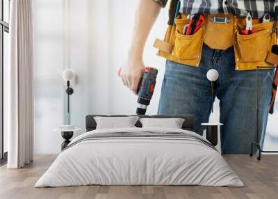 Worker wearing tool belt and holding mobile drill at home Wall mural