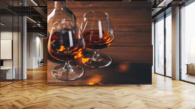 Two glasses of cognac and bottle on the wooden table. Wall mural