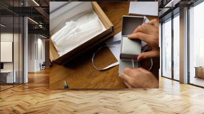 A man unboxing a fashion accessories gift for Valentine's Day, Roth holiday, Christmas, or birthday from a cardboard parcel, revealing a jewelry box inside with a silk bow, highlighting the excitement Wall mural