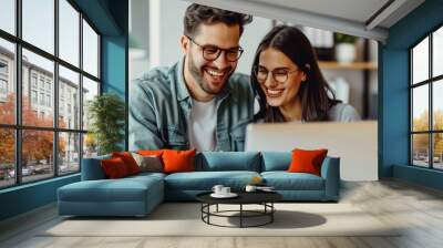 A photo of two happy white people in casual , sitting at a desk and working on a laptop together Wall mural