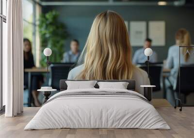 A young woman with long blonde hair is sitting in the foreground, wearing business casual attire and facing away from us towards three people at an office table. Wall mural