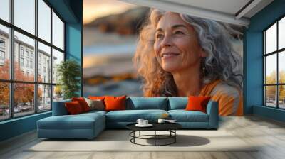 portrait of a beautiful senior woman with grey curly hair smiling and looking at the sky on the beach Wall mural