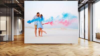 young couple kissing and holding colored smoke in hands, romantic couple with blue color and red color smoke bomb on beach.. Wall mural