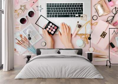 Fashion blogger working with laptop. Workspace with  female accessory, cosmetics products on pale pink table. flat lay, top view Wall mural