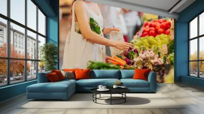 Female hands puts fruits and vegetables in cotton produce bag at food market. Reusable eco bag for shopping. Zero waste concept. Wall mural