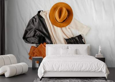 Leather jacket and white warm sweater with brown trousers and hat on white sheet. Women's stylish autumn or winter outfit. Trendy clothes collage. Flat lay, top view. Wall mural