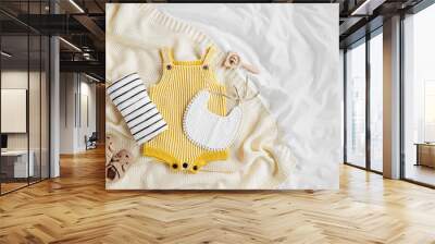 Yellow bodysuit, bib, baby boots and toy on knitted blanket. Set of  kids clothes and accessories  on bed. Fashion newborn. Flat lay, top view Wall mural