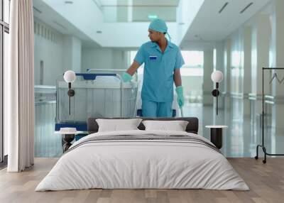 A man in a blue uniform is pushing a cart with a mop in a hospital hallway. Concept of cleanliness and orderliness, as the man is responsible for maintaining the hospital's hygiene Wall mural