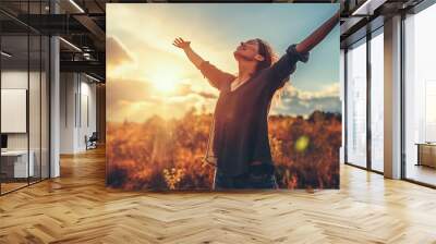 Smiling woman with arms raised in sunset Wall mural