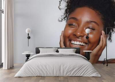 A beautiful woman with radiant skin smiles and touches her face on a white background Wall mural