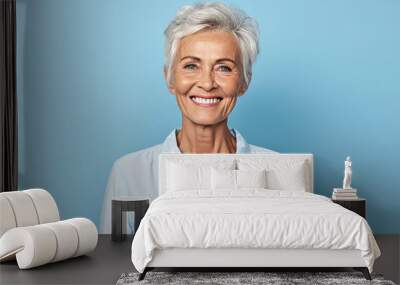 Cheerful mature woman looking at camera and smiling while standing against blue background Wall mural