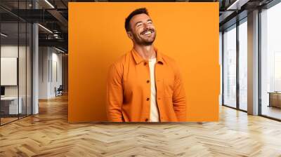 happy young man laughing and looking away on orange background, side view Wall mural