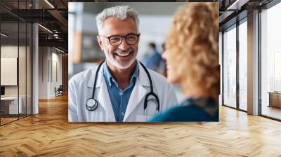 Portrait of senior male doctor with female patient in background at hospital. Doctor and patient discussing something while standing in corridor. Medicine and healthcare concept Wall mural