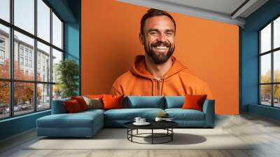 smiling man in orange hoodie looking at camera isolated on orange Wall mural