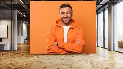 smiling man in orange hoodie with crossed arms isolated on orange Wall mural