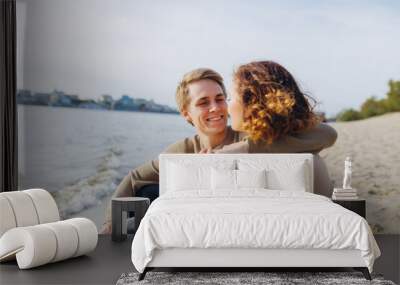 A loving couple has fun - they laugh, hug each other and enjoy a warm summer evening. Romantic couple sitting by the sea. Portrait of a guy hugging his girlfriend Wall mural