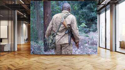 black man in military uniform armed with Kalashnikov walks along path in rainforest, Uganda Wall mural