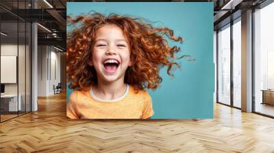 Cute young child  Little girl smiles. Emotion and child development. Little girl smiles while red hair.  A young girl with curly hair is smiling and laughing while wearing a shirt. Wall mural