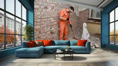 Builder cleaning apartment after demolition jobs, wearing gloves, mask, boots and orange coveralls. Wall mural