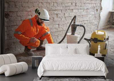 Male constriction site worker cleaning concrete floor from dust with vacuum cleaner after demolishing jobs. Wall mural