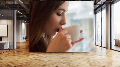  Young girl drinks tea from  smal cup in cafe with big window Wall mural