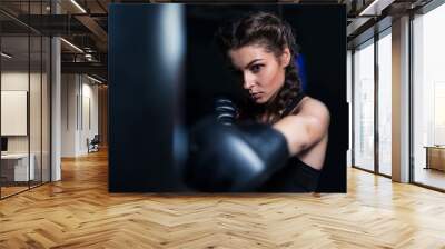 Beautiful fighter boxer fit girl wearing boxing gloves in training with heavy punching bag in gym. Low key image. Woman power Wall mural