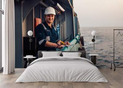 Deck Officer on deck of offshore vessel or ship , wearing PPE personal protective equipment. He fills checklist. Paperwork at sea Wall mural