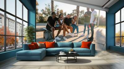 Group of young modern african black friends happily sitting together on the bench of the stairs in bright sunlight enjoying summer vacation Wall mural